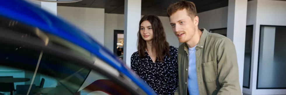 Automotive-Business-test-a-young-couple-stands-near-a-blue-car-in-a-dealership-diffic