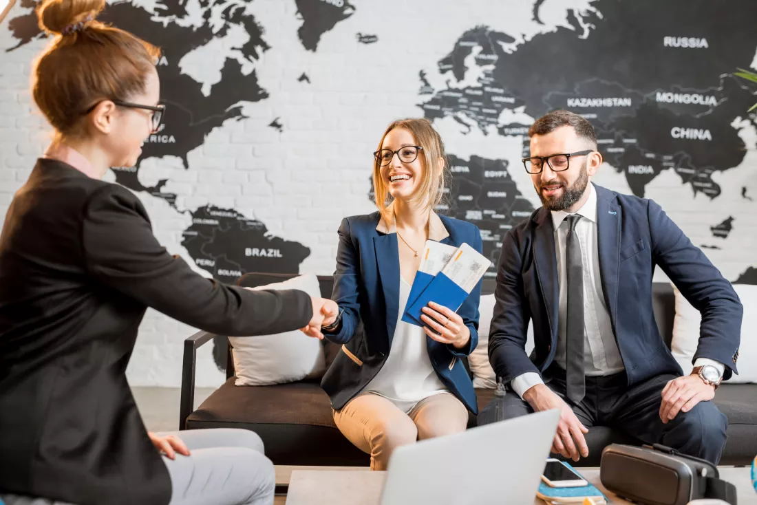 young-businesscouple-choosing-trip-with-agent-sitting-travel-agency-office-with-world-map-background