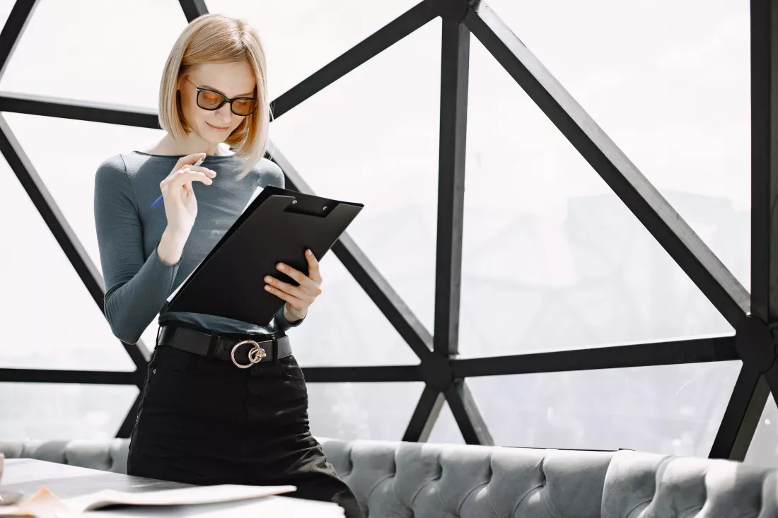 indoor-portrait-young-businesswoman-standing-cafe-writing-paper-holder-blonde-girl-wearing-sunglasses