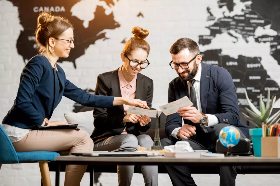 young-businesscouple-choosing-trip-with-agent-sitting-travel-agency-office-with-world-map-background