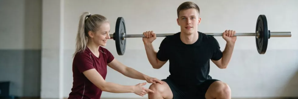 student-coach-correcting-squat-technique-in-a-gym